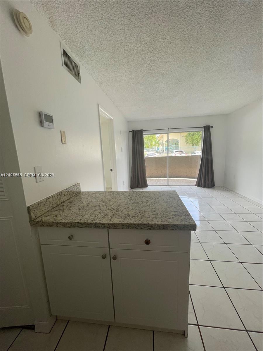A kitchen counter with granite countertops overlooks a living area with tile flooring and curtains — 5199 NW 7th St # 112, Miami FL 33126, MIAMI, FL