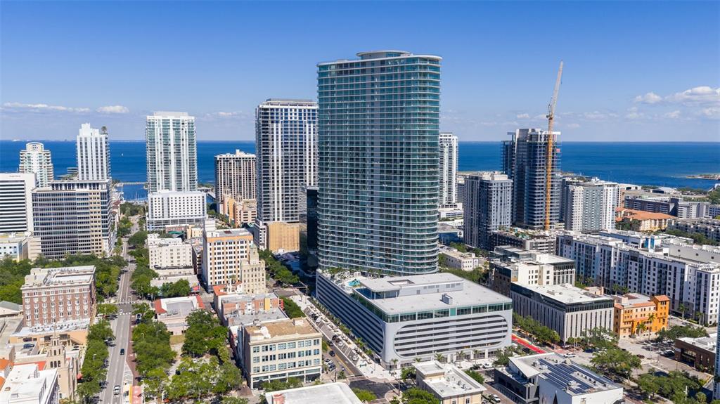 An aerial view shows a tall glass residential tower surrounded by other buildings and water — 400 CENTRAL AVENUE UNIT 3906, ST PETERSBURG, FL