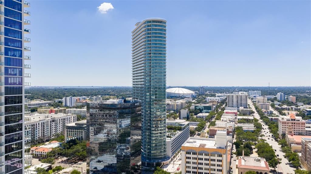An aerial view shows a tall glass residential tower surrounded by city buildings and streets — 400 CENTRAL AVENUE UNIT 3906, ST PETERSBURG, FL