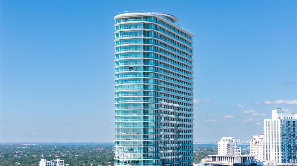A tall, modern glass residential skyscraper stands against a clear blue sky — 400 CENTRAL AVENUE UNIT 3906, ST PETERSBURG, FL