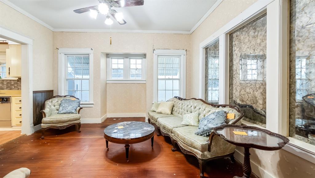 A living room features hardwood floors, vintage furniture, wallpaper, and large windows with mirrored panels — 127 E LAUREL AVENUE, HOWEY IN THE HILLS, FL