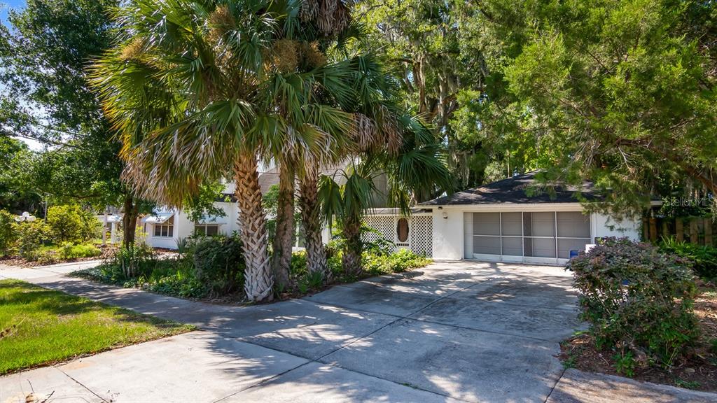 A white house features a concrete driveway, a two-car garage, and several tall palm trees — 127 E LAUREL AVENUE, HOWEY IN THE HILLS, FL