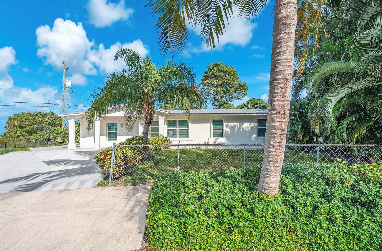 A single-story house with a white exterior, a palm tree, and a chain-link fence — 3308 E El Vedado Court, West Palm Beach FL 33405, WEST PALM BEACH, FL
