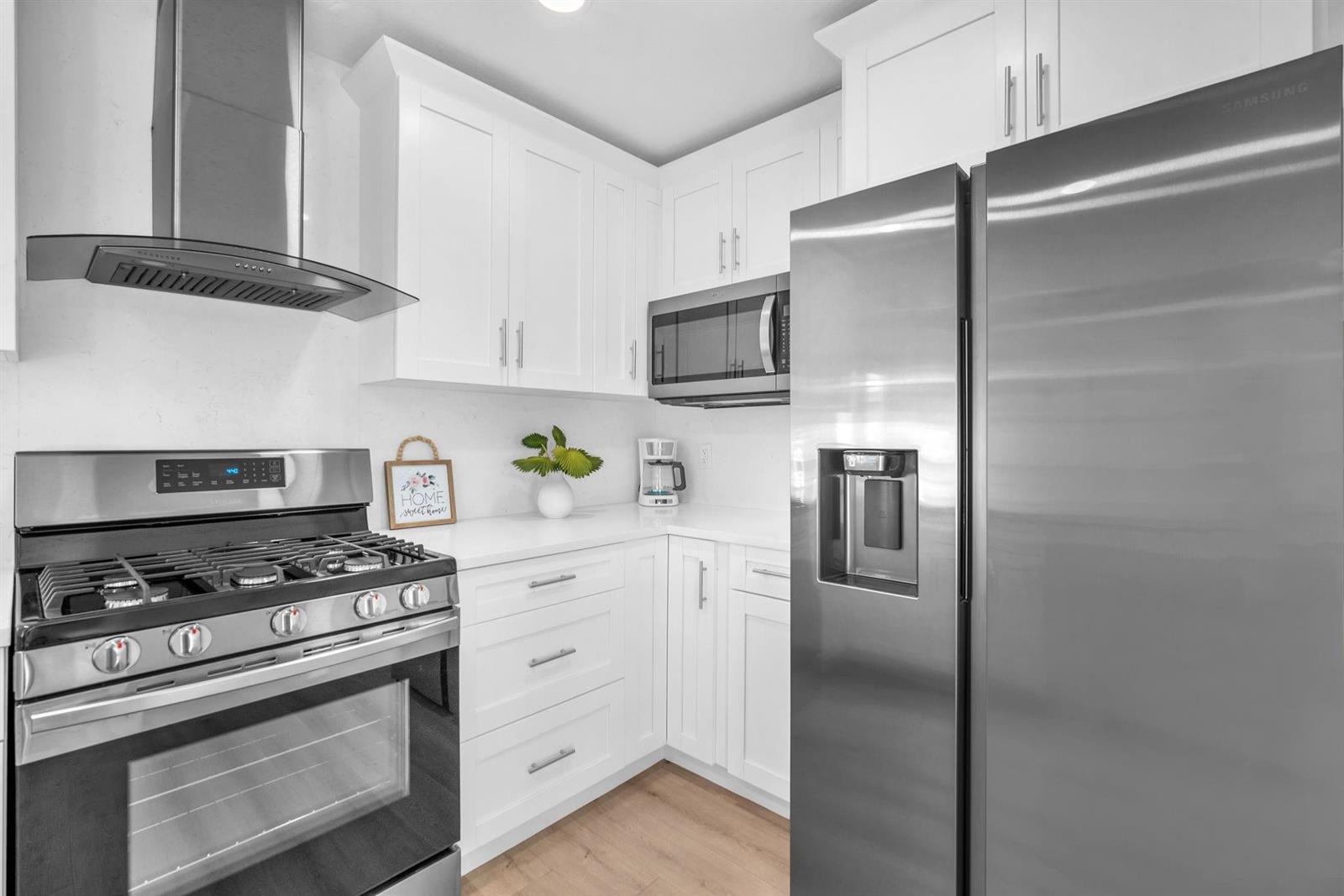 A modern kitchen features white cabinets, stainless steel appliances, and light wood-look flooring — 3308 E El Vedado Court, West Palm Beach FL 33405, WEST PALM BEACH, FL