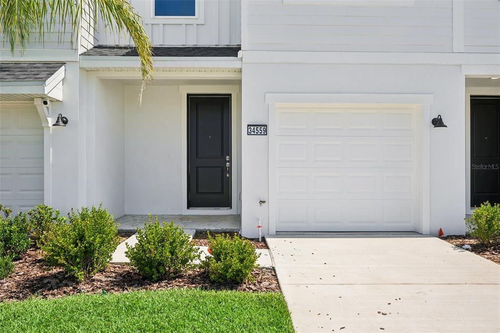 The exterior of a white townhouse features a black front door and a single-car garage — 34559 TURPINS AVENUE, ZEPHYRHILLS, FL