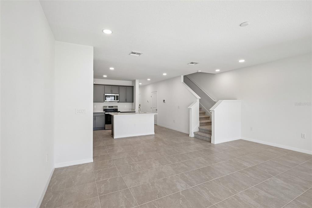 An open-concept living area features light tile flooring, a kitchen with dark cabinets, and stairs — 34559 TURPINS AVENUE, ZEPHYRHILLS, FL