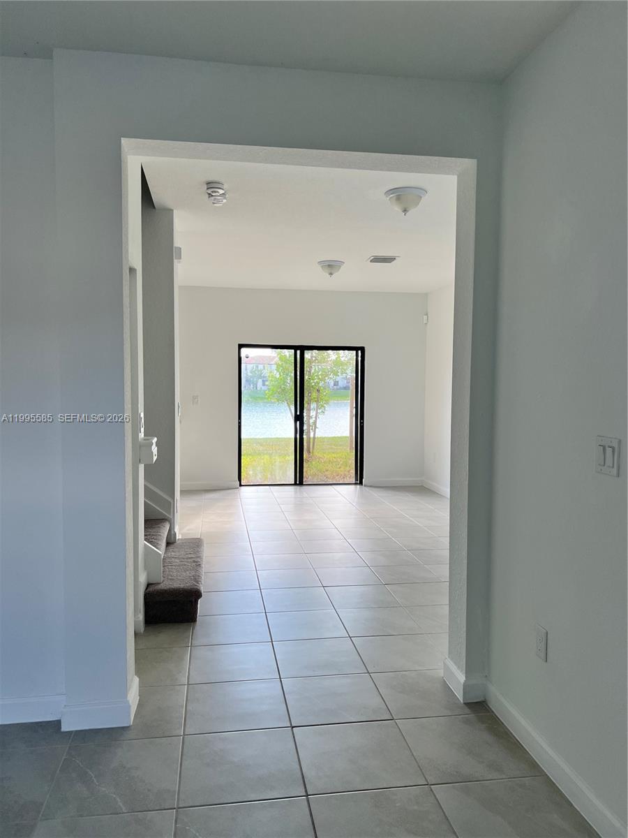 A tiled room leads to sliding glass doors with a view of a lake — 10030 SW 228th Ter, Miami FL 33190, MIAMI, FL