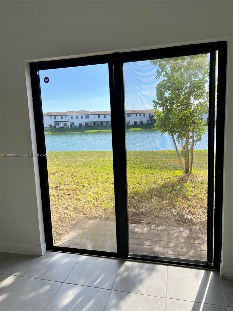 A sliding glass door offers a view of a lake and townhomes from a room — 10030 SW 228th Ter, Miami FL 33190, MIAMI, FL