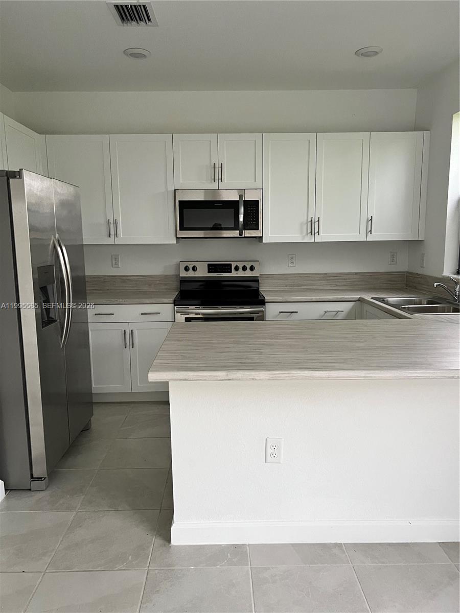 A kitchen features white cabinets, stainless steel appliances, and light-colored wood-look countertops — 10030 SW 228th Ter, Miami FL 33190, MIAMI, FL