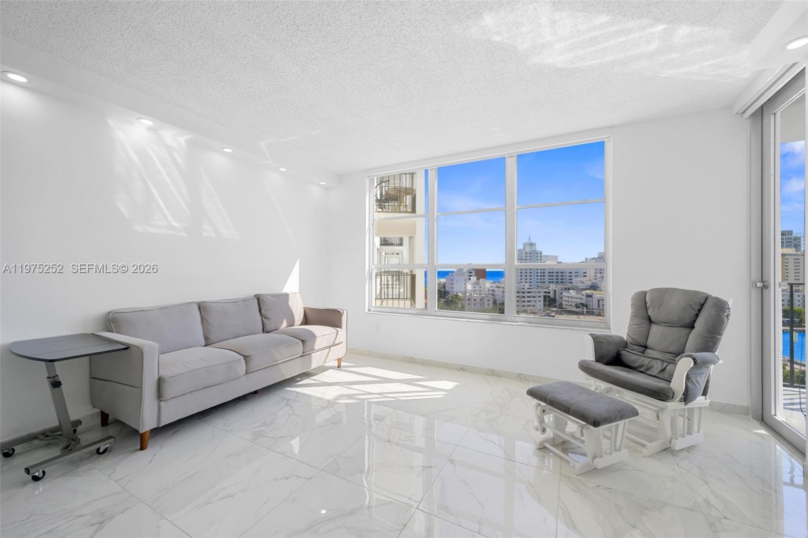 A living room with white marble floors, a gray sofa, a rocking chair, and ocean views — 4101 Pine Tree Dr # 919, Miami Beach FL 33140, MIAMI BEACH, FL