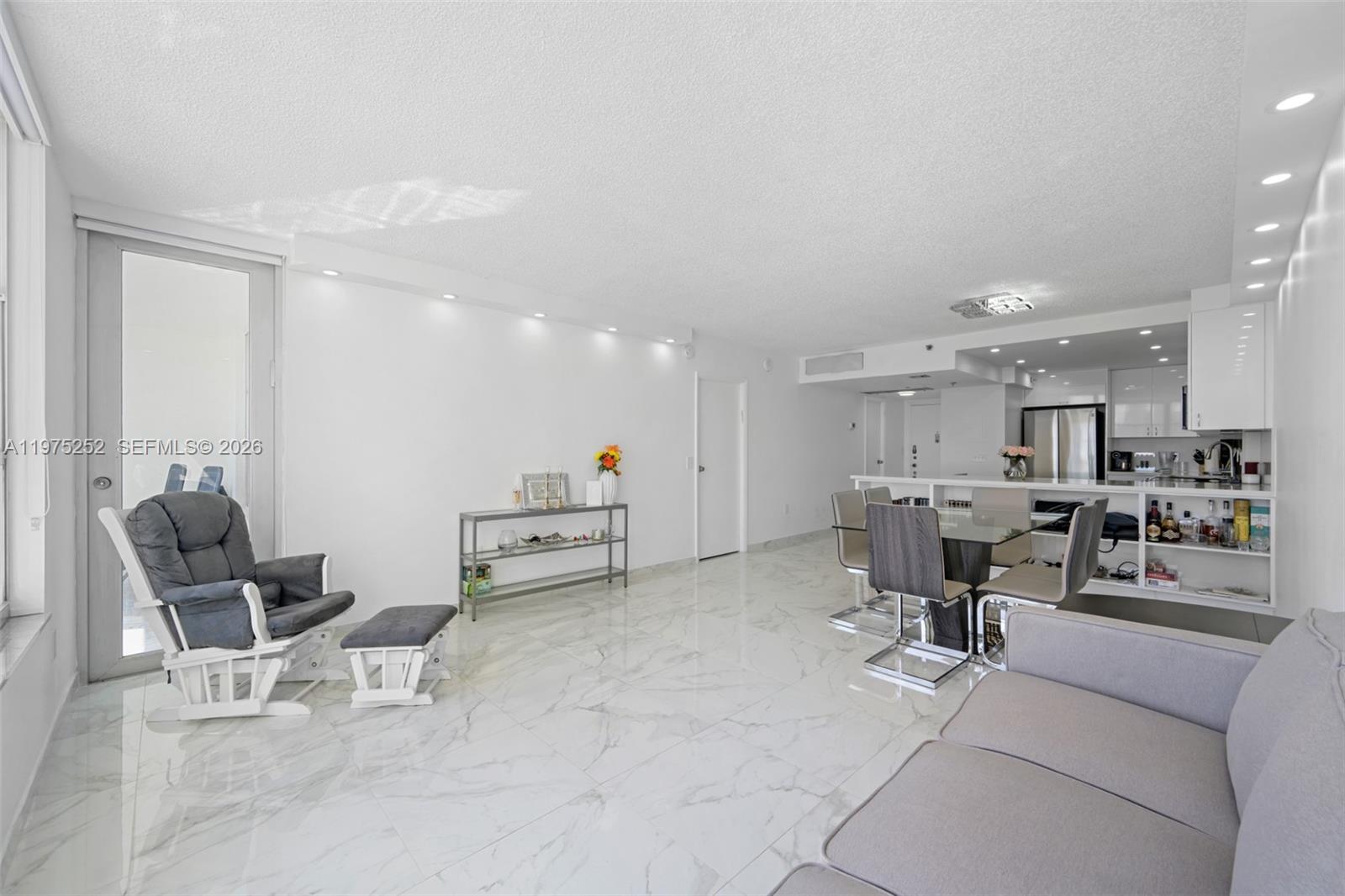 A bright, open-concept living and dining area features white marble flooring and recessed lighting — 4101 Pine Tree Dr # 919, Miami Beach FL 33140, MIAMI BEACH, FL