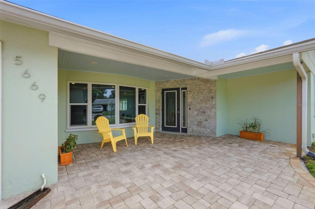 A paved patio features two yellow chairs in front of a house with stone accents — 5669 45TH AVENUE N, KENNETH CITY, FL