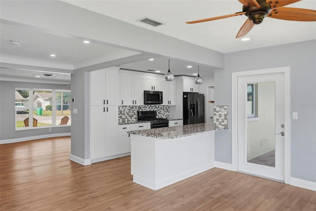 A kitchen with white cabinets, granite countertops, and a breakfast bar opens to a living area — 5669 45TH AVENUE N, KENNETH CITY, FL