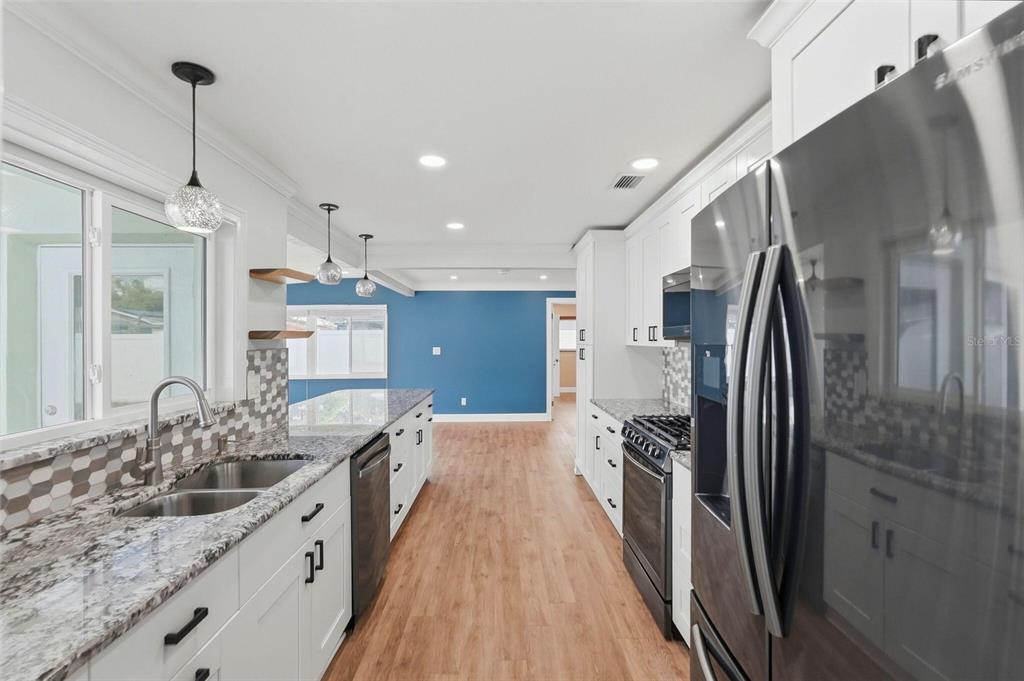 A modern kitchen features white cabinets, granite countertops, stainless steel appliances, and a blue wall — 5669 45TH AVENUE N, KENNETH CITY, FL