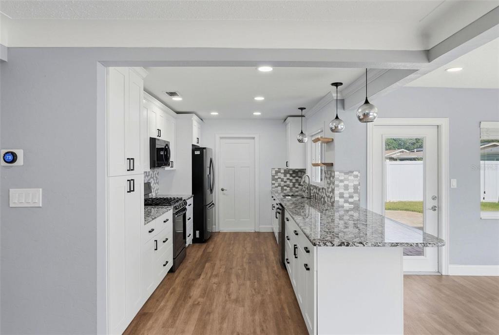 A modern kitchen features white cabinetry, granite countertops, stainless steel appliances, and wood-look flooring — 5669 45TH AVENUE N, KENNETH CITY, FL
