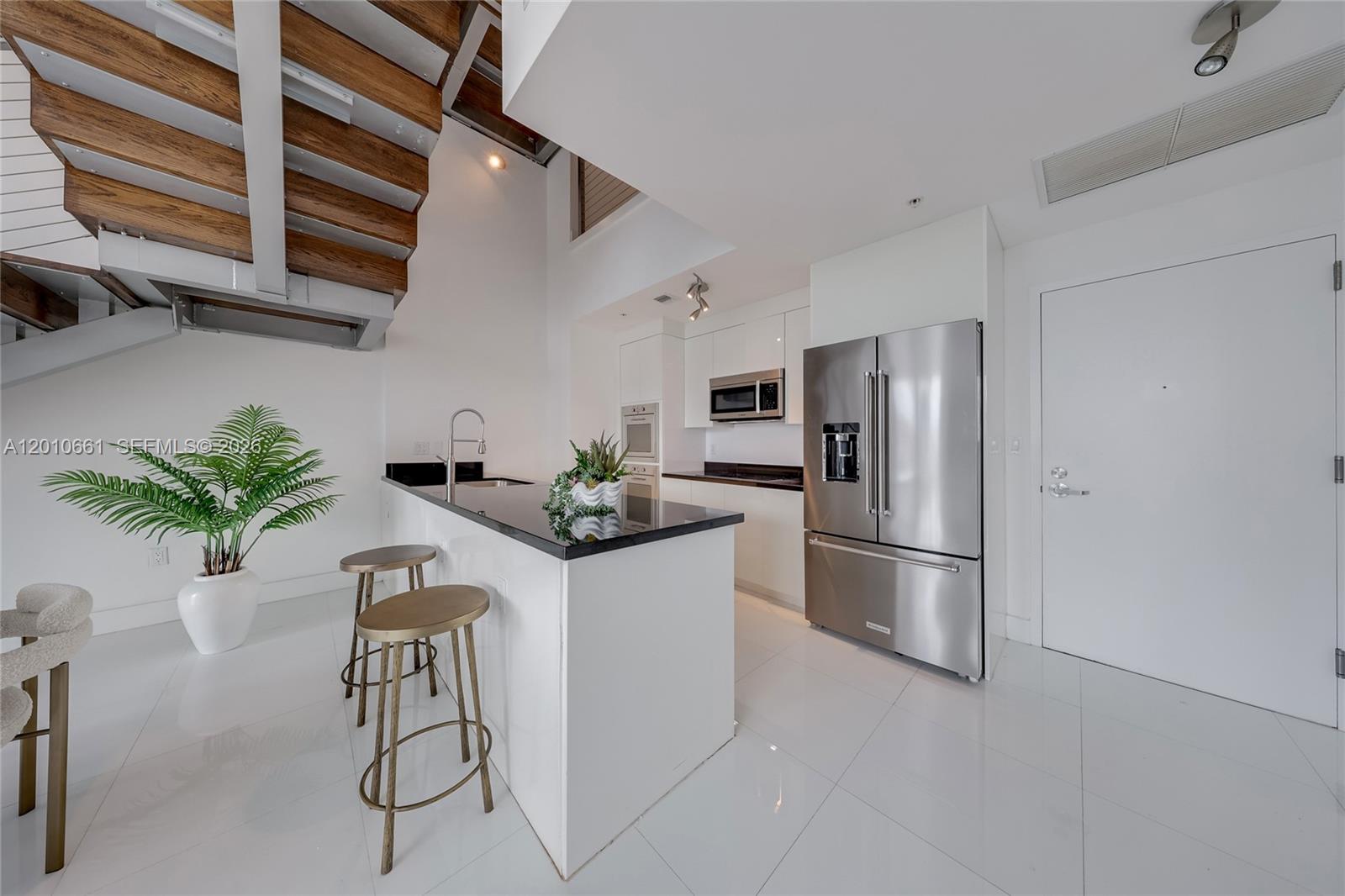 A modern kitchen features white cabinetry, black countertops, stainless steel appliances, and a wooden staircase — 92 SW 3rd St # 5202, Miami FL 33130, MIAMI, FL