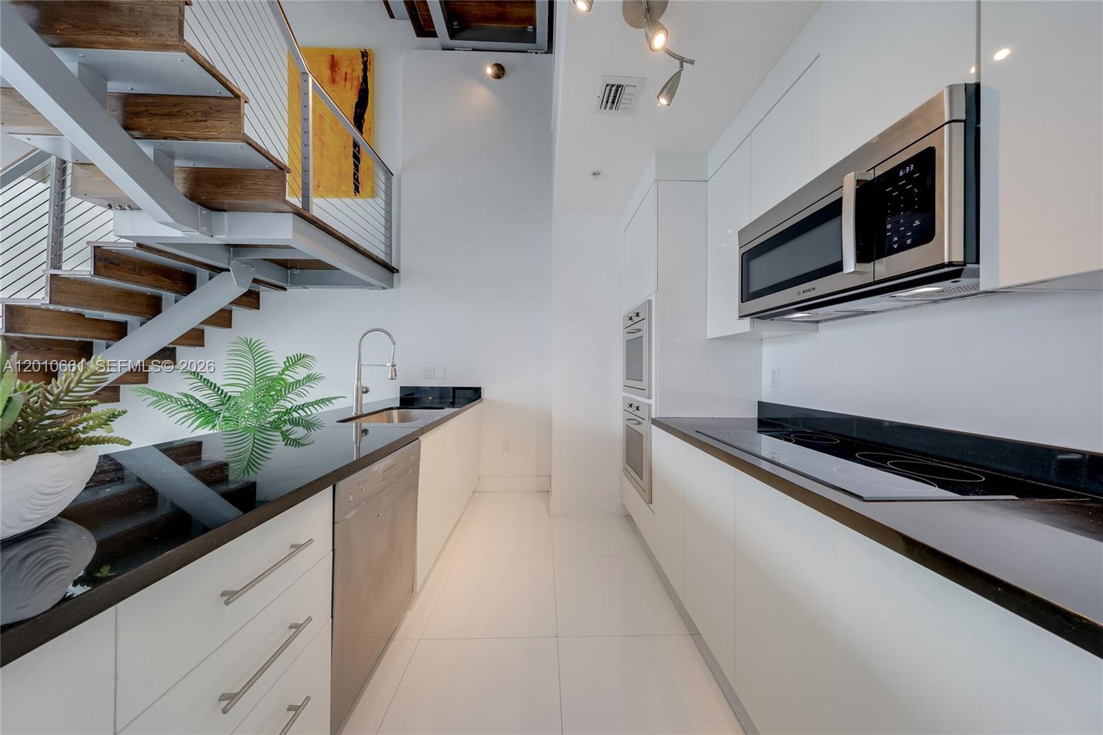 A modern galley kitchen features white cabinets, black countertops, stainless appliances, and an adjacent staircase — 92 SW 3rd St # 5202, Miami FL 33130, MIAMI, FL