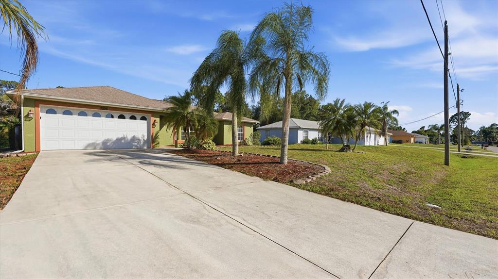 A single-story house with a green exterior, a white garage door, and several palm trees — 3196 CIRCLEVILLE STREET, NORTH PORT, FL
