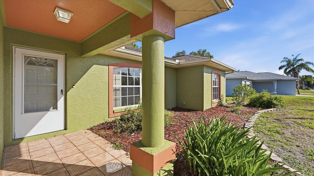 A green house exterior features a tiled front porch, a column, and a white door — 3196 CIRCLEVILLE STREET, NORTH PORT, FL