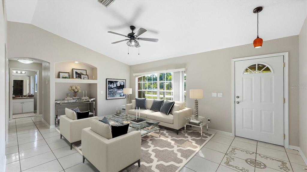 A bright living room features a vaulted ceiling, tiled floors, and a white front door — 3196 CIRCLEVILLE STREET, NORTH PORT, FL