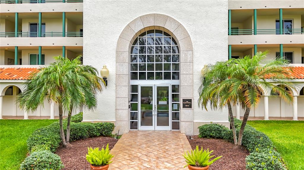The exterior of a multi-story building features a central arched entrance with glass doors — 4801 OSPREY DRIVE S UNIT 103, ST PETERSBURG, FL