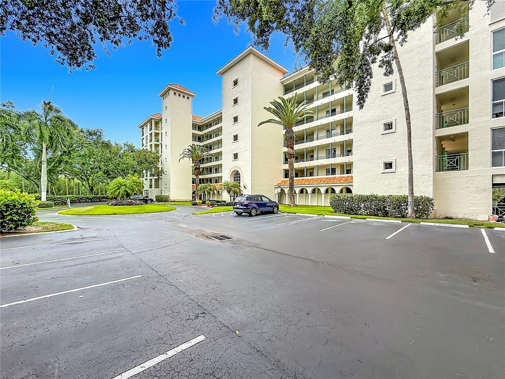 A multi-story beige apartment building features balconies and a parking lot in the foreground — 4801 OSPREY DRIVE S UNIT 103, ST PETERSBURG, FL