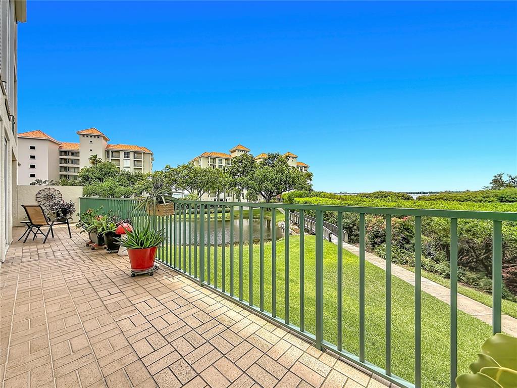 A tiled balcony with a green metal railing overlooks a grassy lawn and a pond — 4801 OSPREY DRIVE S UNIT 103, ST PETERSBURG, FL
