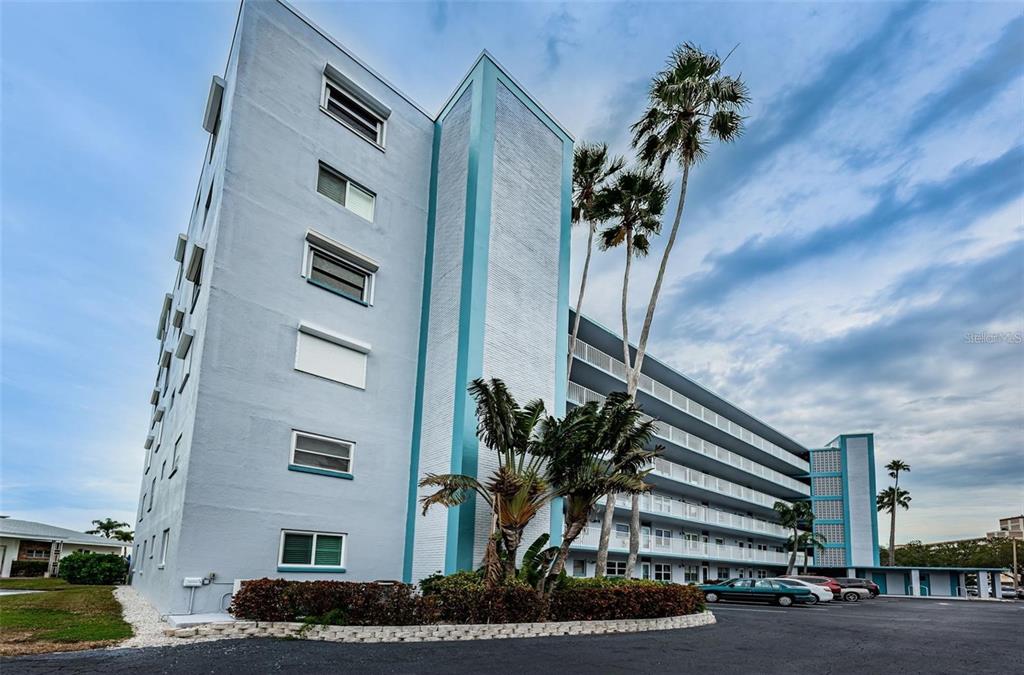 A low-angle exterior view of a multi-story apartment building with palm trees and parking — 1868 SHORE DRIVE S UNIT 102, SOUTH PASADENA, FL