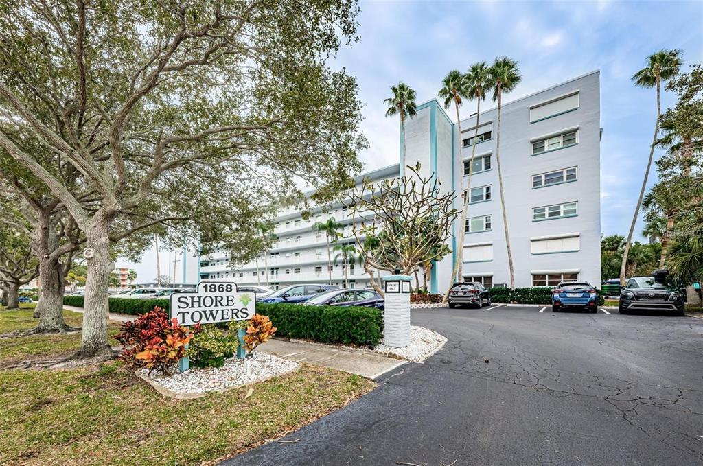 A multi-story apartment building with a sign in the foreground and a parking lot — 1868 SHORE DRIVE S UNIT 102, SOUTH PASADENA, FL