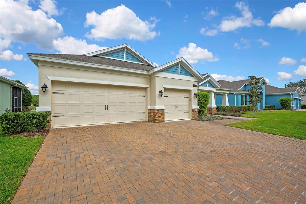 A beige house with a brick paver driveway and a three-car garage under a blue sky — 19863 TATTNALL WAY, BROOKSVILLE, FL