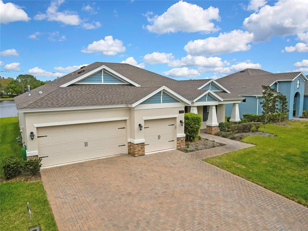 A beige house with a three-car garage and blue gables sits on a paved driveway — 19863 TATTNALL WAY, BROOKSVILLE, FL