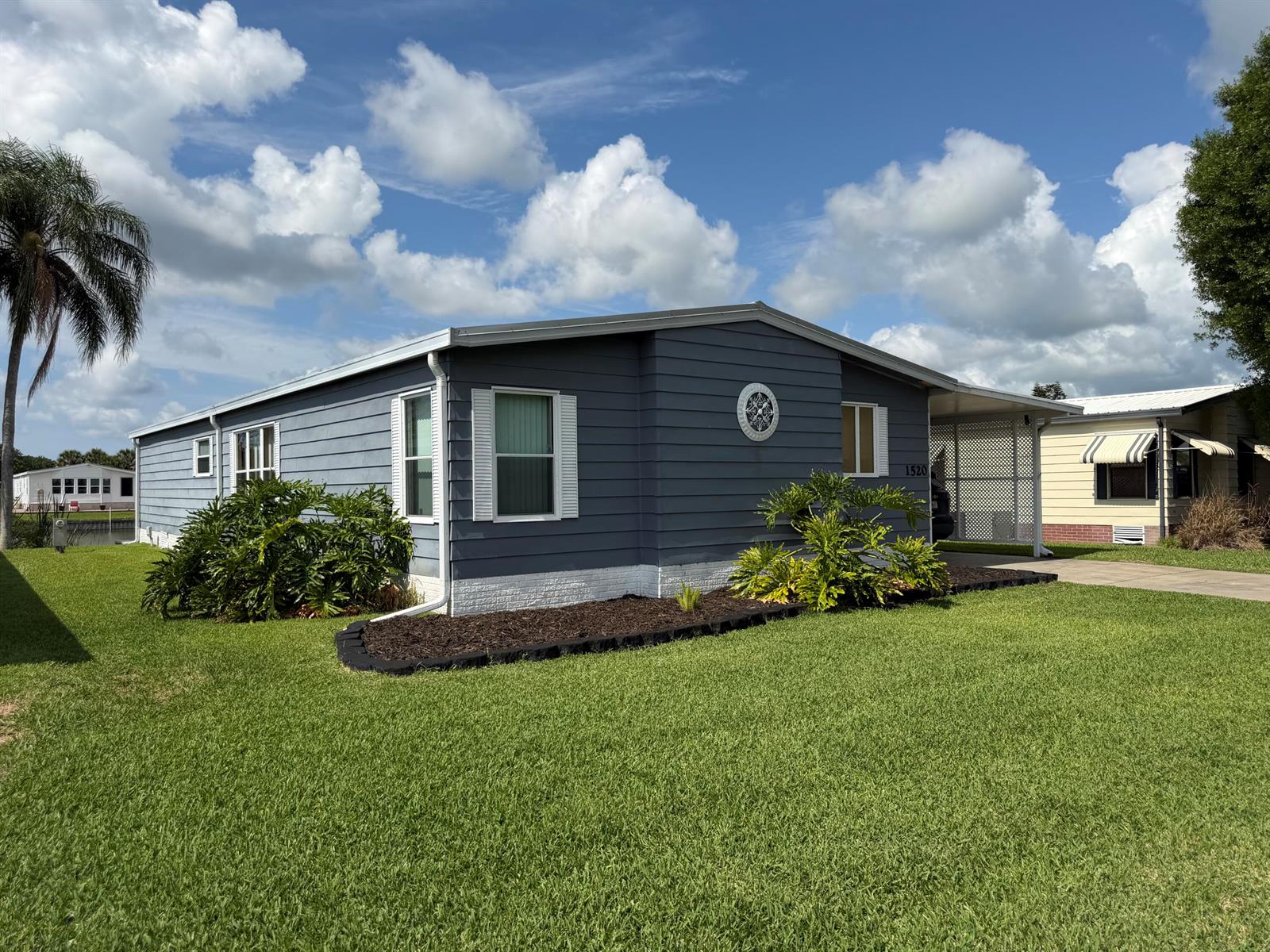 A blue mobile home with white trim, a carport, and landscaping sits on a lawn — 1520 SW 35th Circle, Okeechobee FL 34974, OKEECHOBEE, FL