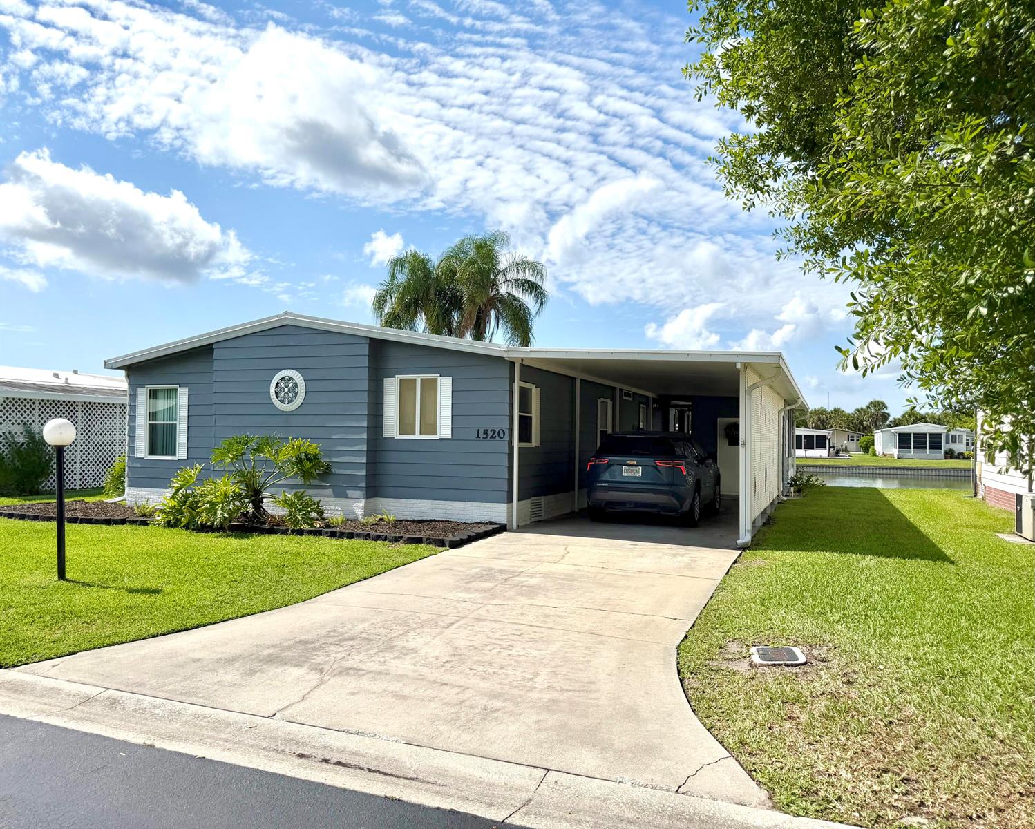 A blue single-story house with a carport and driveway sits on a grassy lot — 1520 SW 35th Circle, Okeechobee FL 34974, OKEECHOBEE, FL