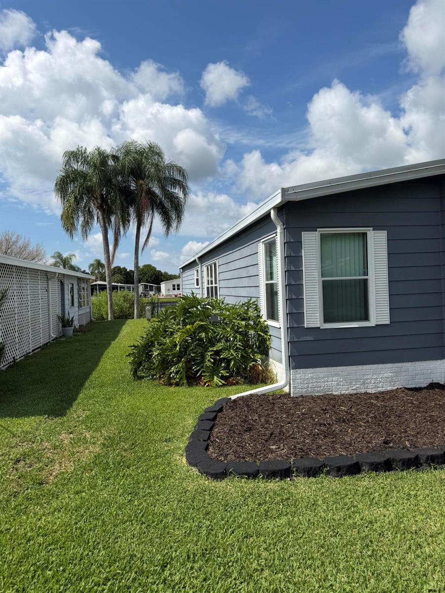 A blue-sided mobile home exterior features a landscaped mulch bed and a grassy side yard — 1520 SW 35th Circle, Okeechobee FL 34974, OKEECHOBEE, FL