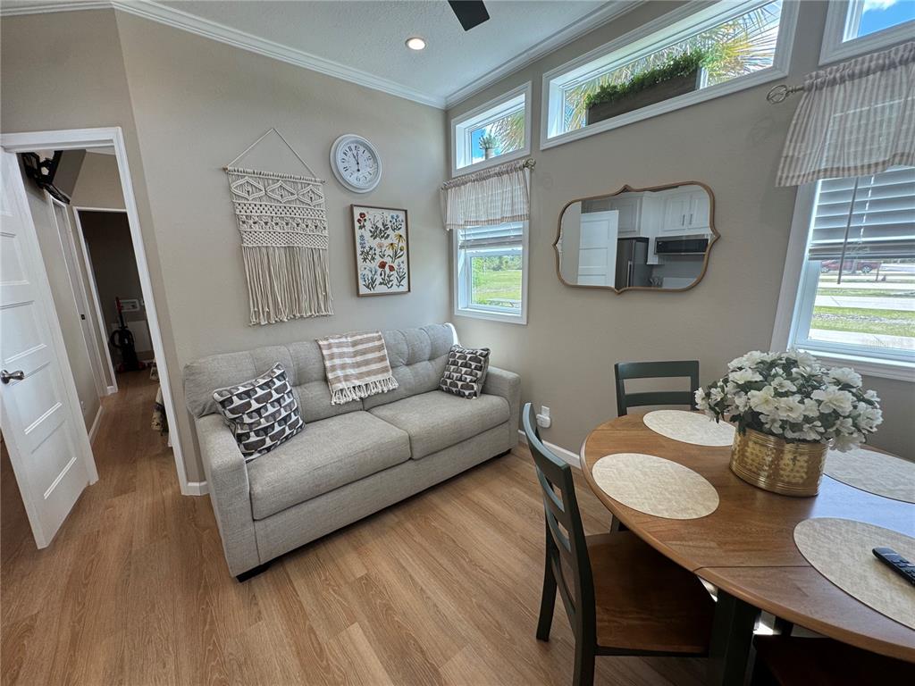 A living and dining area features a gray sofa, a round wooden table, and windows — 16950 HIGHWAY 630E UNIT 140, LAKE WALES, FL