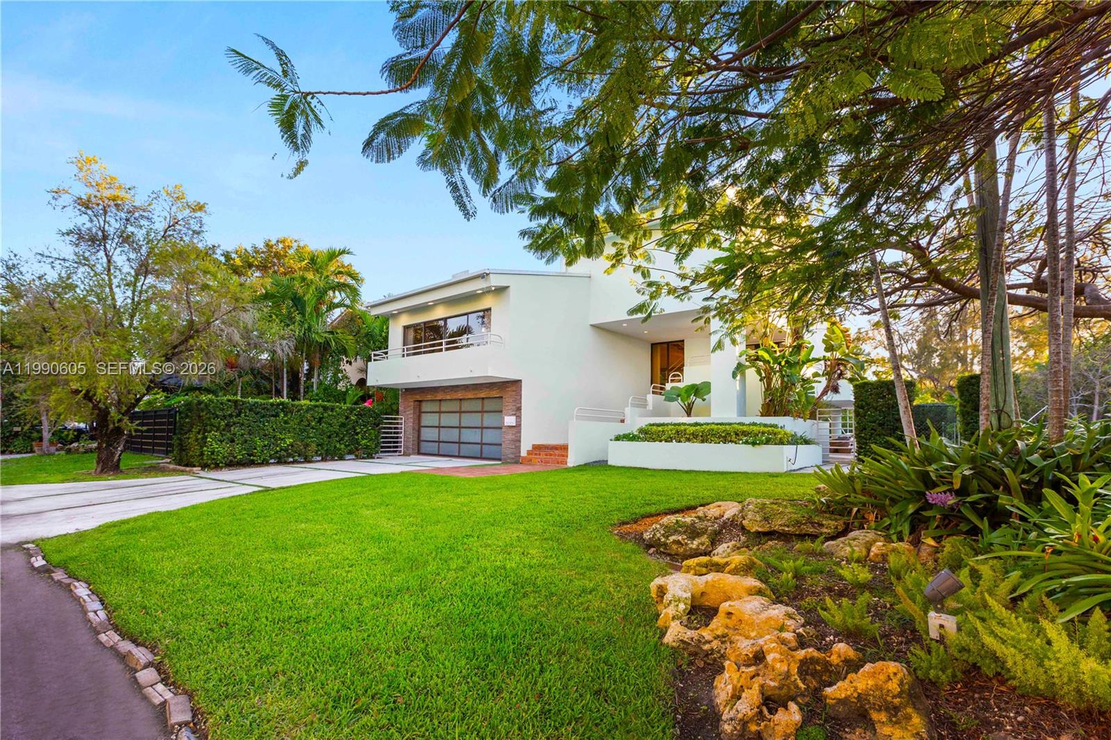 A modern two-story house with a garage and landscaped lawn sits under large trees — 3520 Rockerman Rd, Miami FL 33133, MIAMI, FL