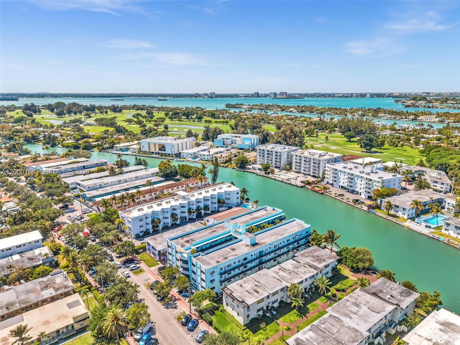 An aerial view shows multi-story apartment buildings situated along a canal near a golf course — 1165 Marseille Dr # 9, Miami Beach FL 33141, MIAMI BEACH, FL