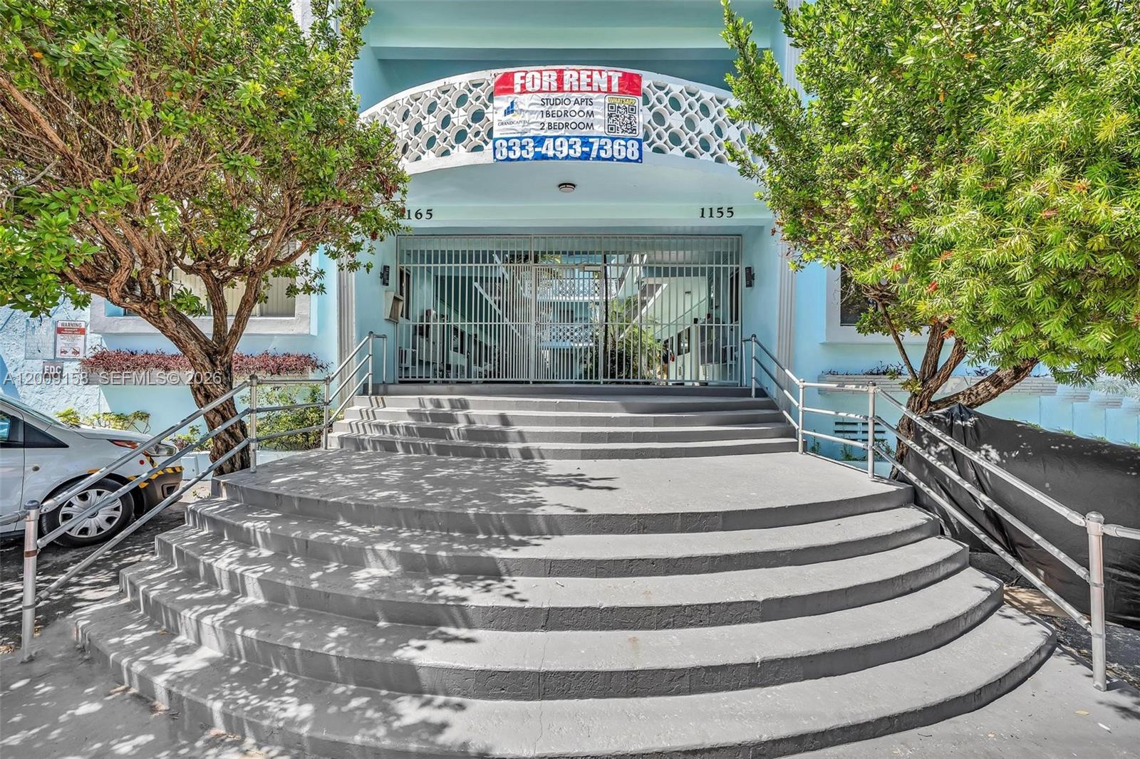 The exterior of a light blue apartment building features curved concrete steps leading to a gate — 1165 Marseille Dr # 9, Miami Beach FL 33141, MIAMI BEACH, FL