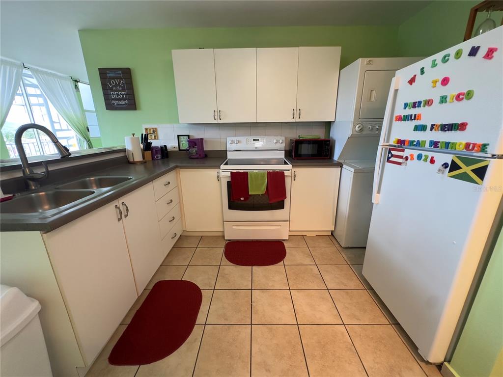 A kitchen features white cabinetry, a white stove, a stacked washer-dryer, and tiled flooring — 500 CALLE SAN PATRICIO Apt D 402, FAJARDO, PR
