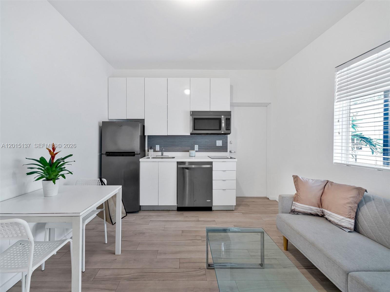 A small kitchen with white cabinets and stainless steel appliances sits beside a living area — 820 15th St # 202, Miami Beach FL 33139, MIAMI BEACH, FL