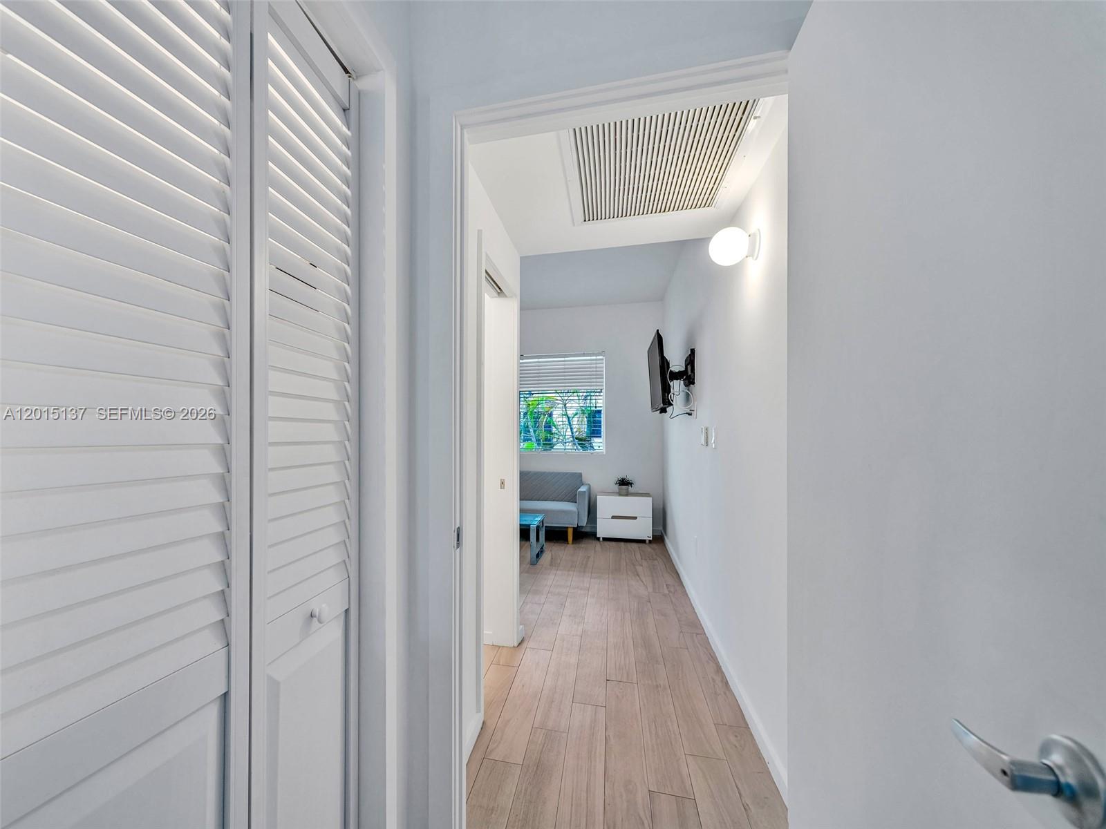 A hallway with wood-look flooring leads into a small room with a window and sofa — 820 15th St # 202, Miami Beach FL 33139, MIAMI BEACH, FL