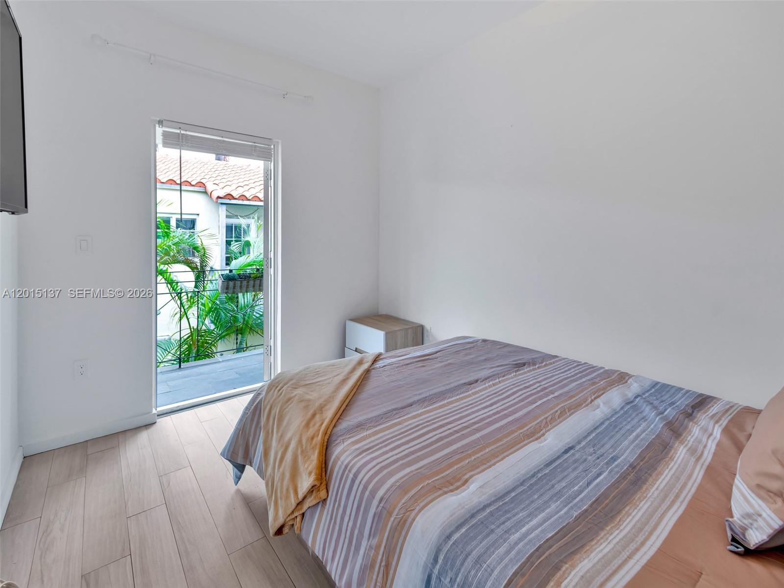 A bedroom features light wood-look flooring, a bed with striped bedding, and a glass door — 820 15th St # 202, Miami Beach FL 33139, MIAMI BEACH, FL