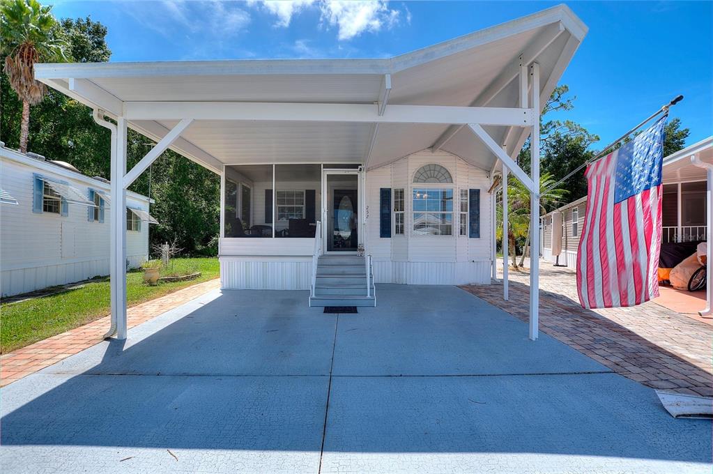 A white manufactured home features a large covered carport, a screened porch, and an American flag — 252 CITRUS RIDGE DRIVE, DAVENPORT, FL