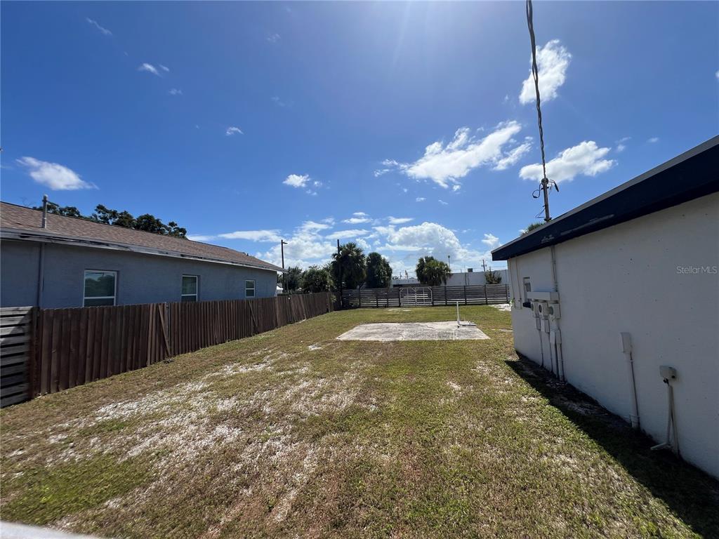 A grassy backyard features a concrete slab, a wooden fence, and two adjacent house exteriors — 1713 N ALBANY AVENUE, TAMPA, FL