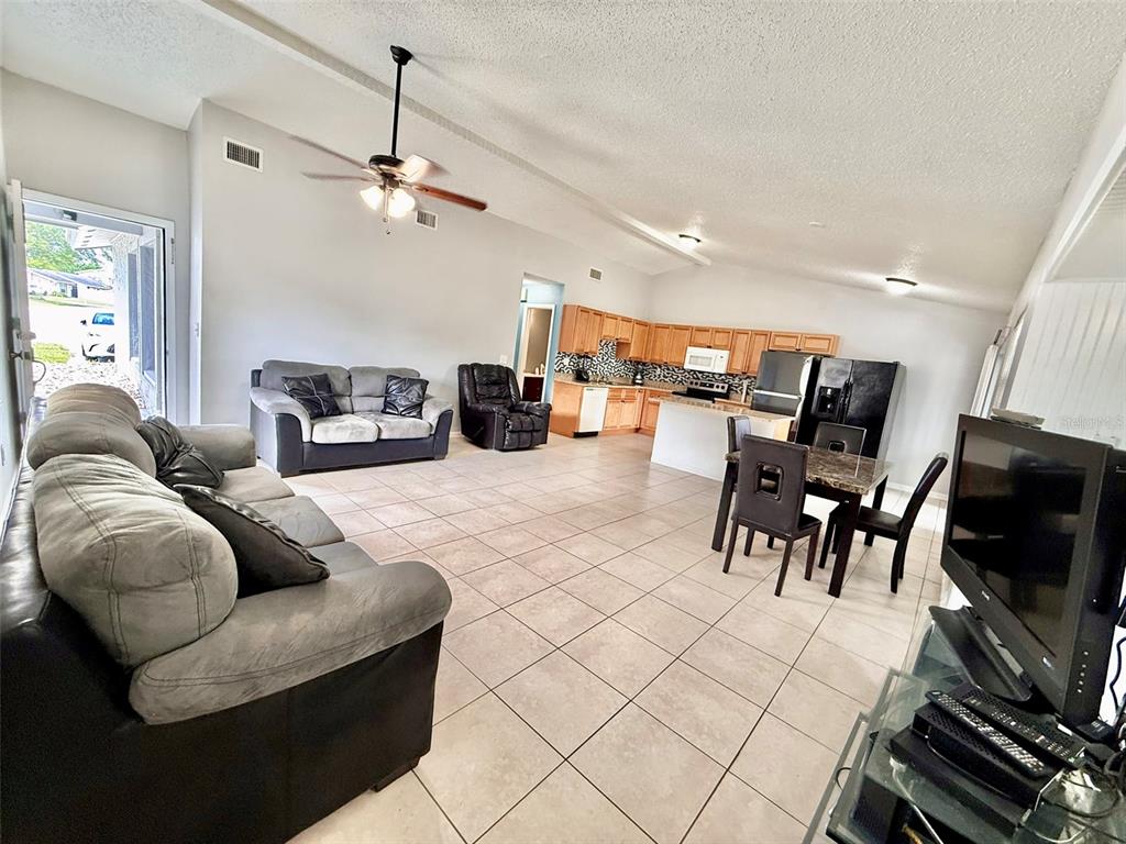 An open-concept living room and kitchen featuring tile flooring, light gray walls, and vaulted ceilings — 10309 PARKCREST DRIVE, TAMPA, FL