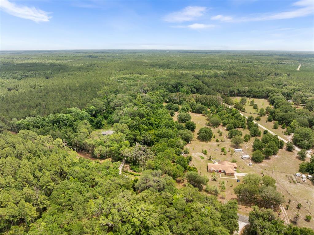 An aerial view shows a house and outbuildings situated on a large, wooded rural lot — 2919 SE COUNTY ROAD 234, GAINESVILLE, FL