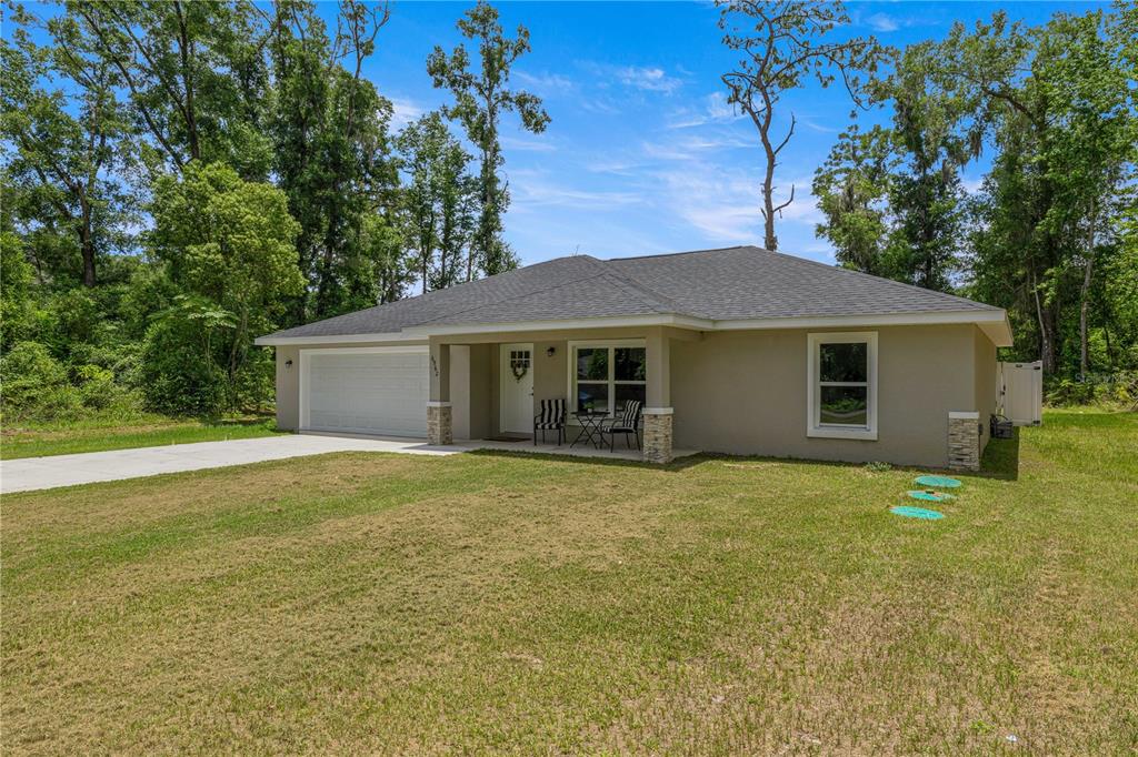 A single-story tan house with a two-car garage and stone accents sits on a grassy lot — 6962 SE 124TH STREET, BELLEVIEW, FL