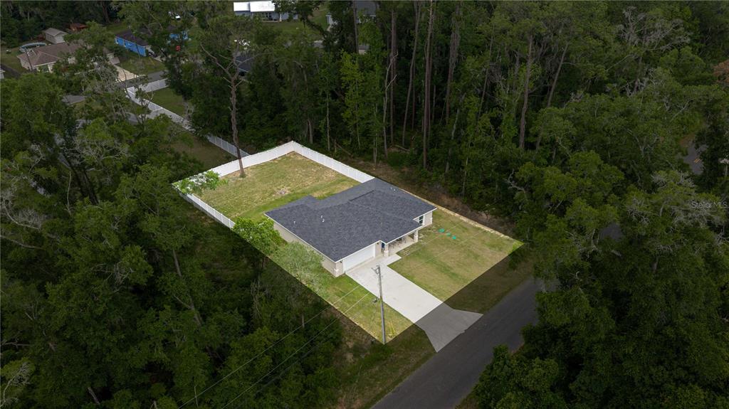 An aerial view shows a single-story house with a fenced backyard surrounded by dense woods — 6962 SE 124TH STREET, BELLEVIEW, FL