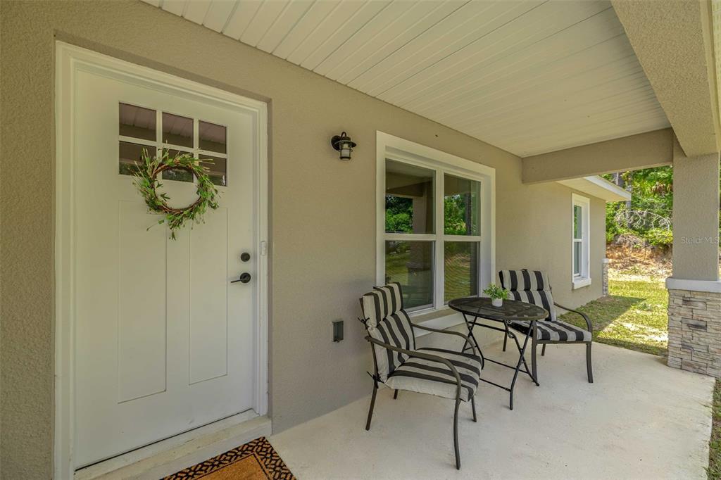 A covered front porch features a white door with a wreath and two striped chairs — 6962 SE 124TH STREET, BELLEVIEW, FL