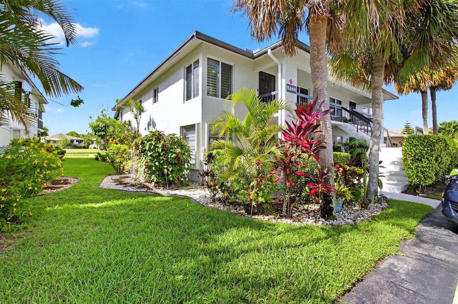 A two-story white apartment building features a landscaped lawn and tropical plants — 5844 Areca Palm Ct., Unit B, Delray Beach FL 33484, DELRAY BEACH, FL
